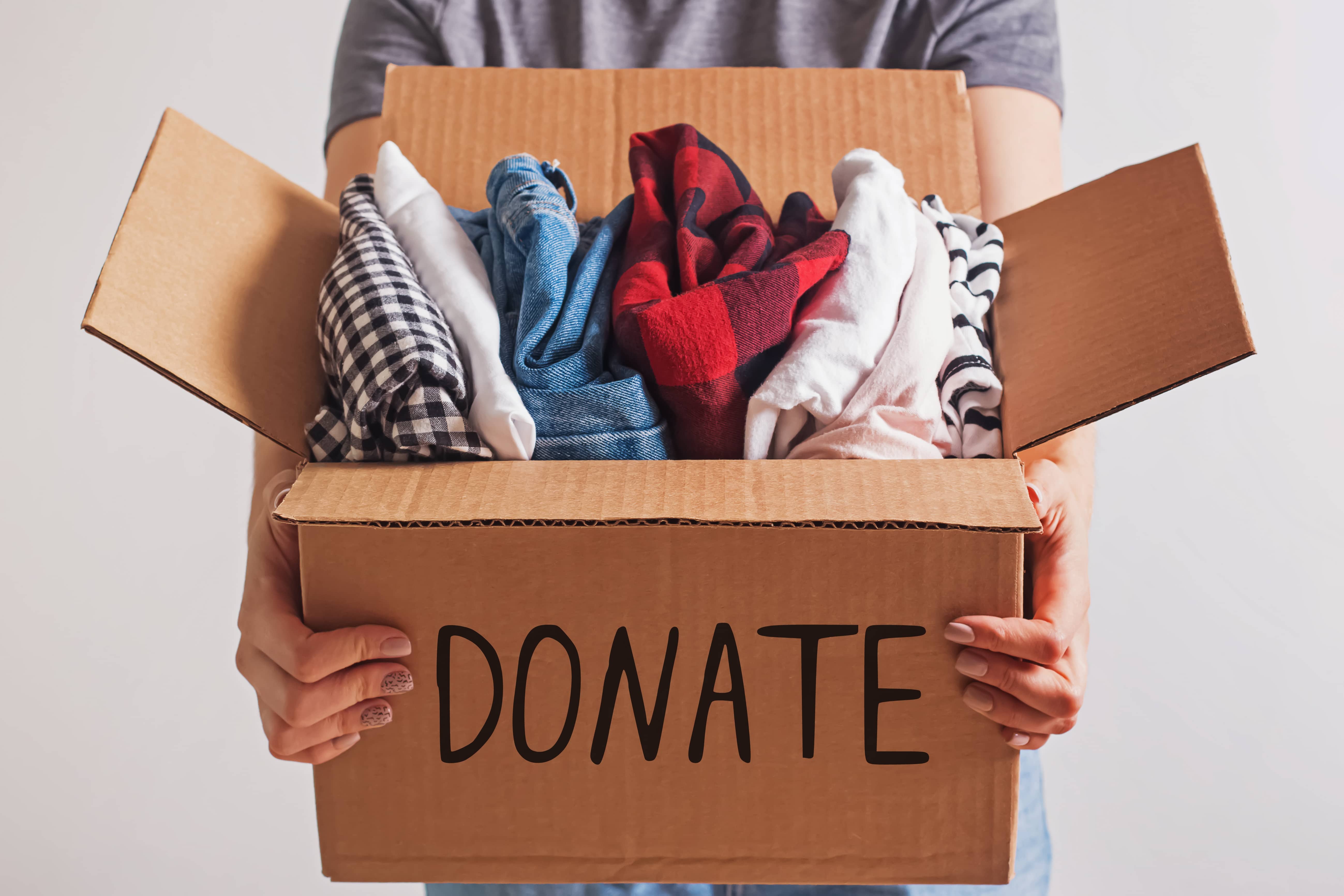 Woman holding a box with clothing close up with donate written on the side of the box