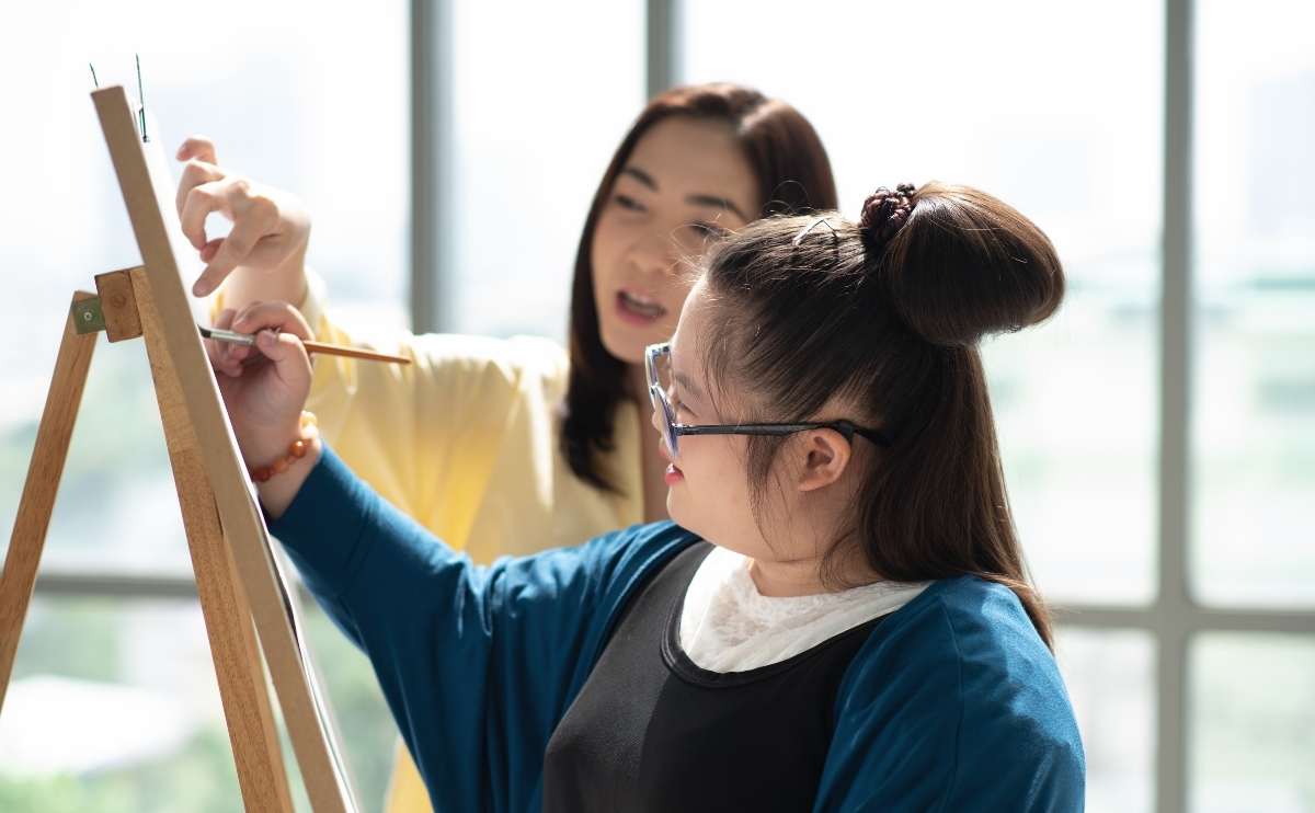 An autistic girl practicing drawing and painting with her mother at home.