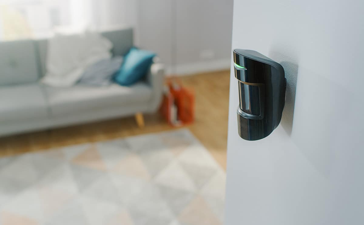 Close up image of black motion sensor on a white wall with a modern apartment in the background.