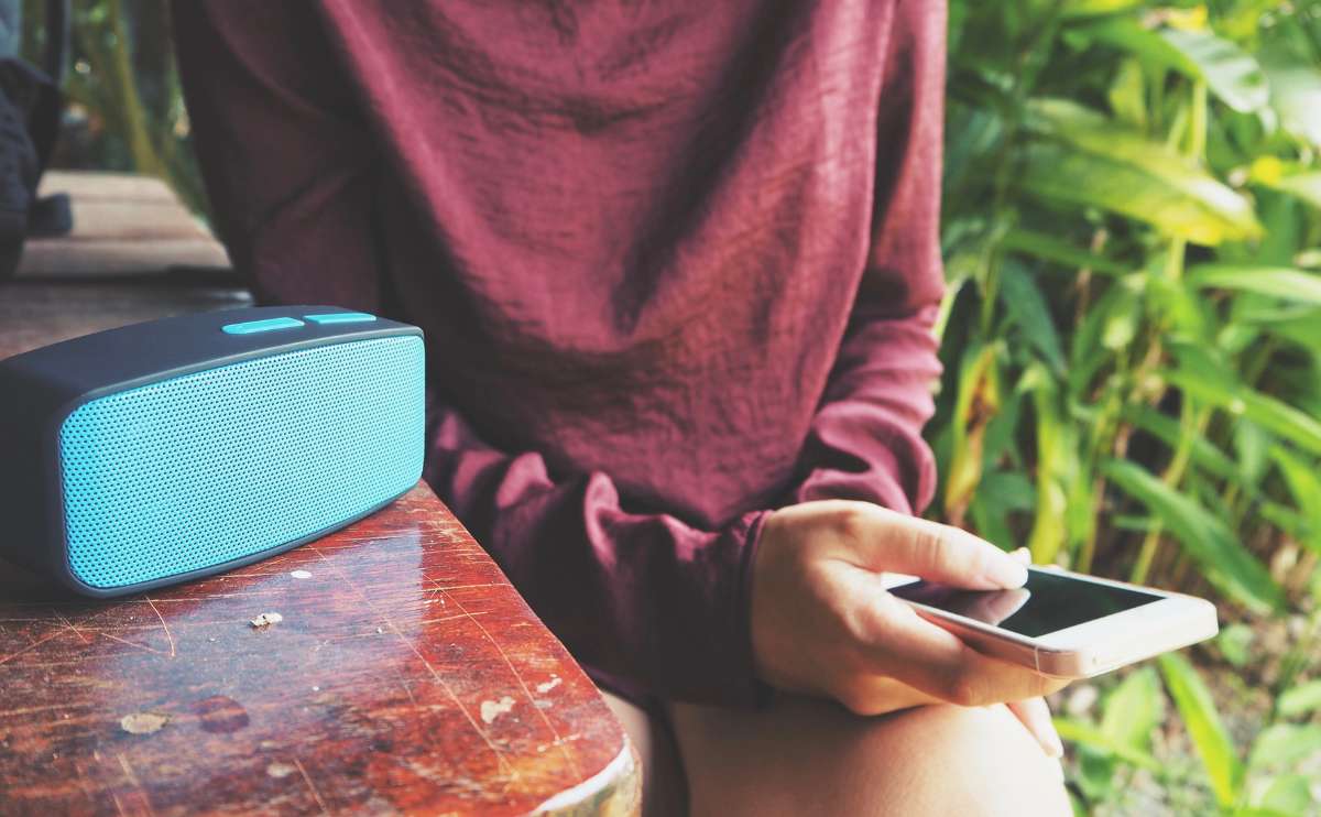 Bluetooth speaker outside on a table with a girl syncing her phone to play music sitting next to it.