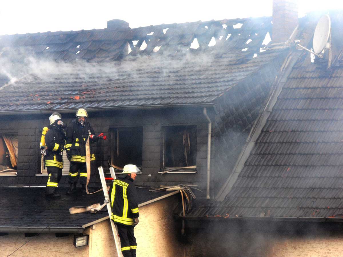 Charred house from fire with firefighters climbing in upstairs window.