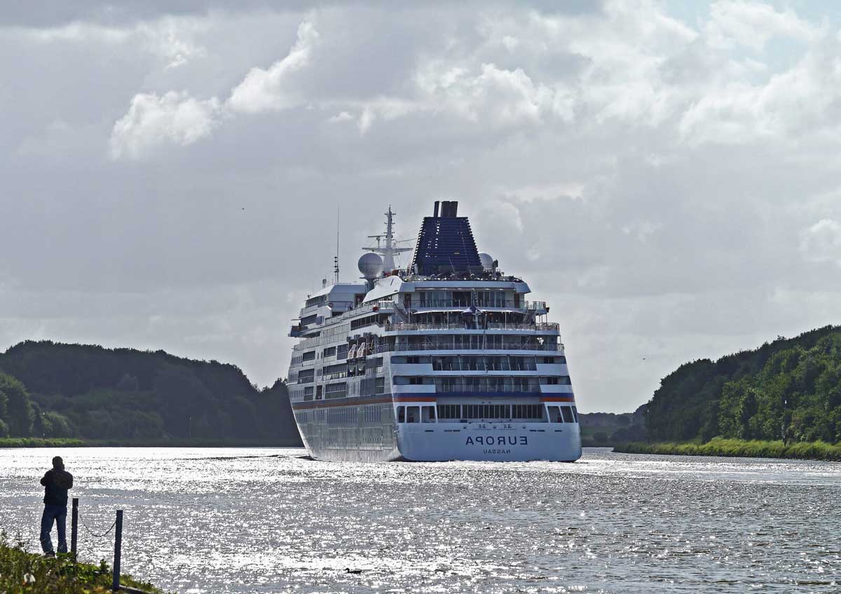 Europa Aassau cruise ship in water with onlooker bottom left and green hills on both sides