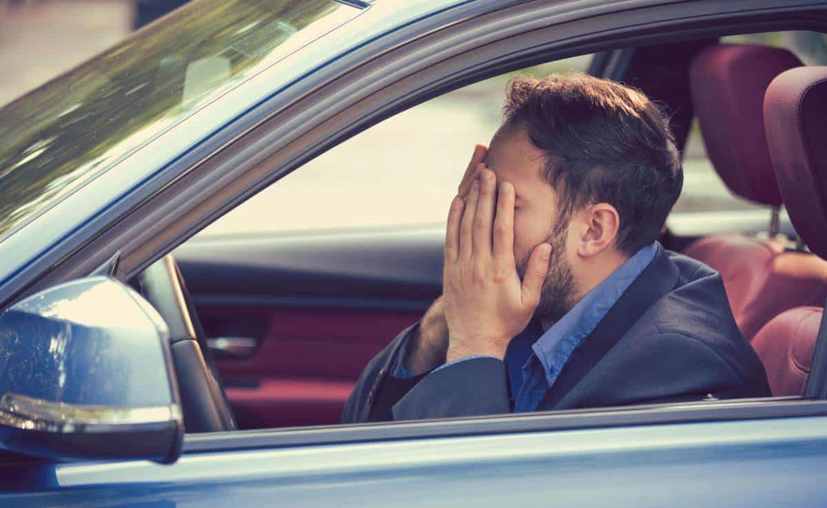 young man sitting inside his car and feeling stressed and upset with hands on face