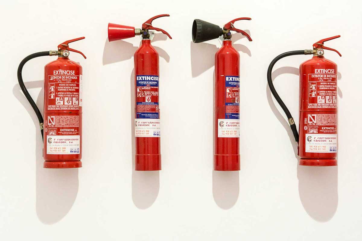 Four red fire extinguishers with symbols and instructions