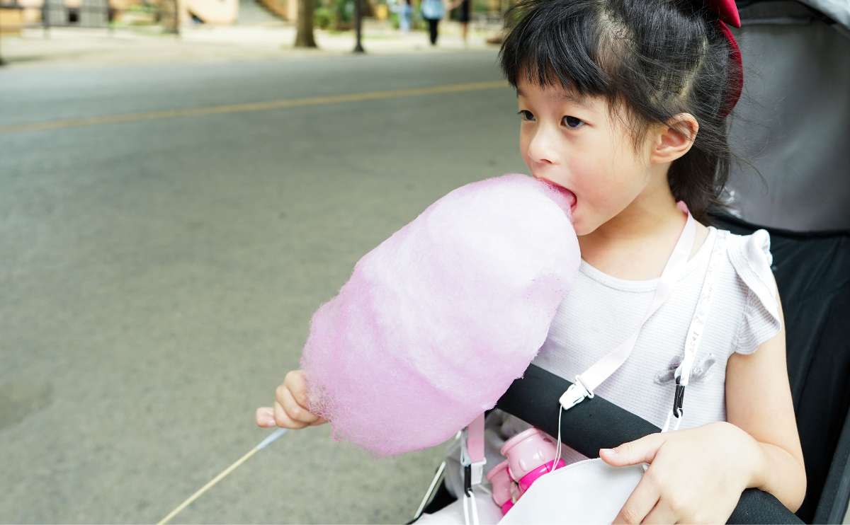 Grl sitting in baby stroller with pink cotton candy eating candy.