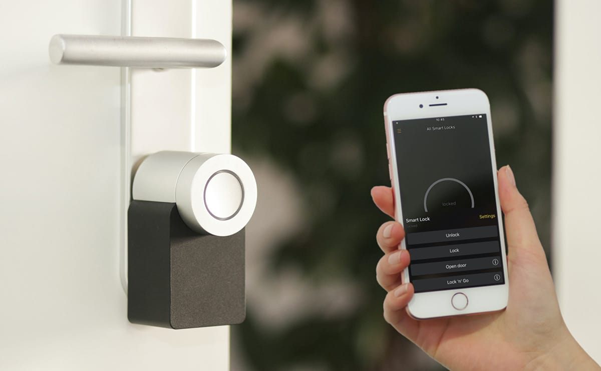 A handing holding a cellphone in front of smart lock. A smart lock app is open on phone. 