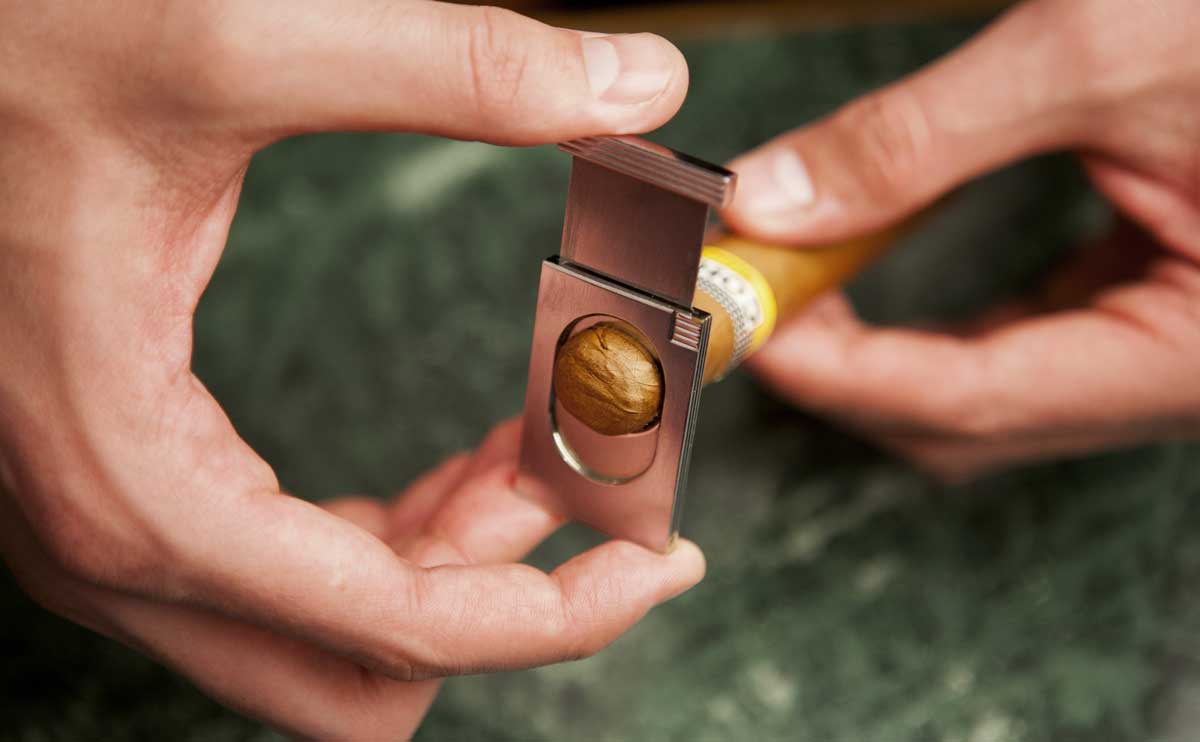 Close-up of hand using cigar cutter to cut cigar