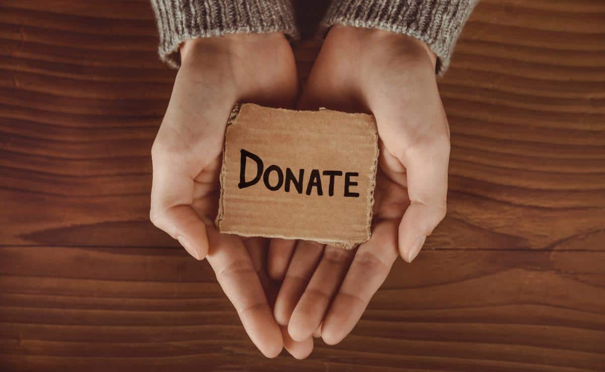 Hands cupped together holding a donation sign written on cardboard.