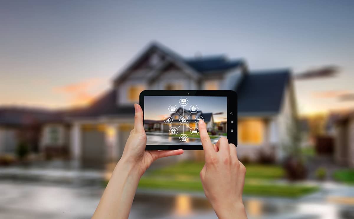 Hands holding up a home security control panel in front of house. 