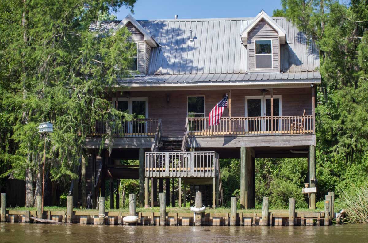 House on river flanked by trees with American flag on deck