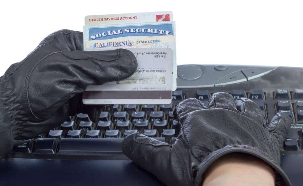 Gloved hands holding a social security card in the left hand while typing on a keyboard with the right hand