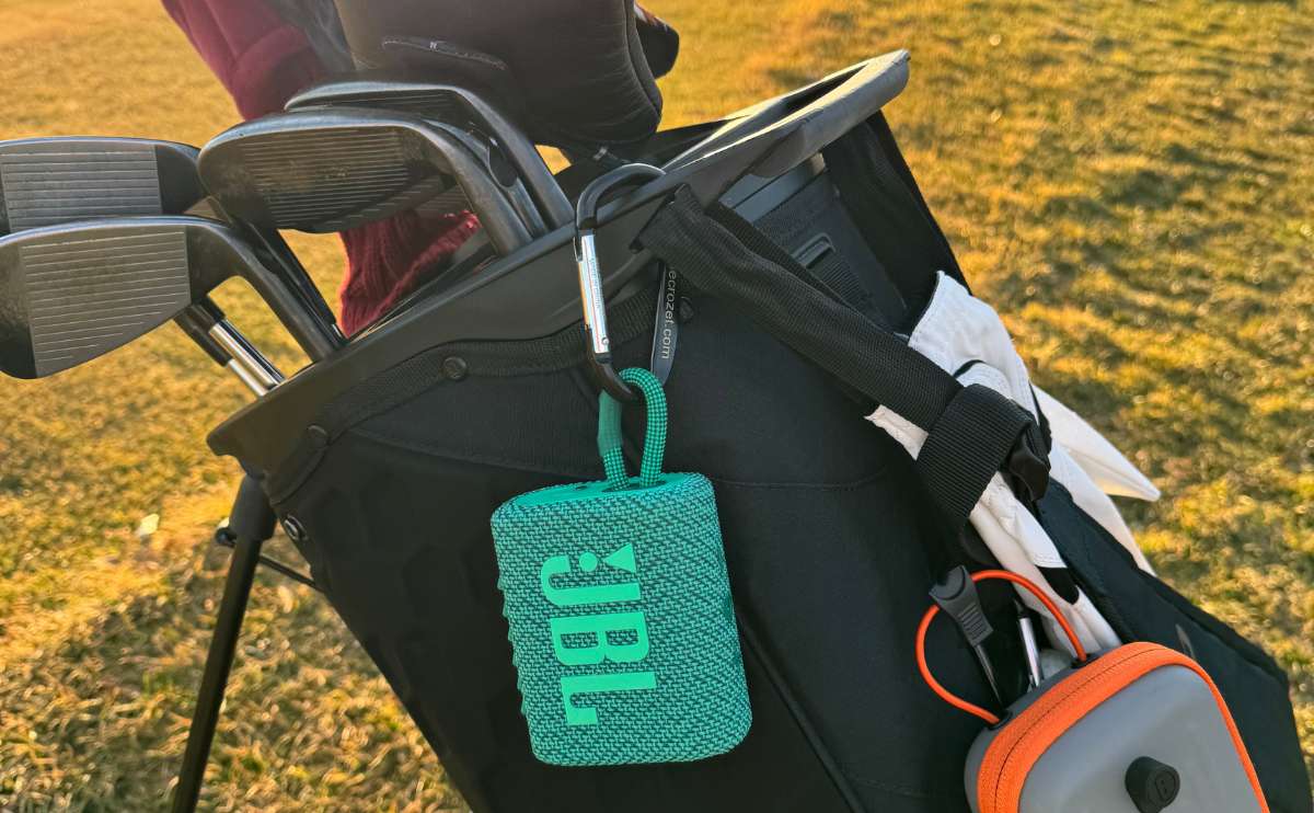 JBL go in green attached to golf clubs outside on course.