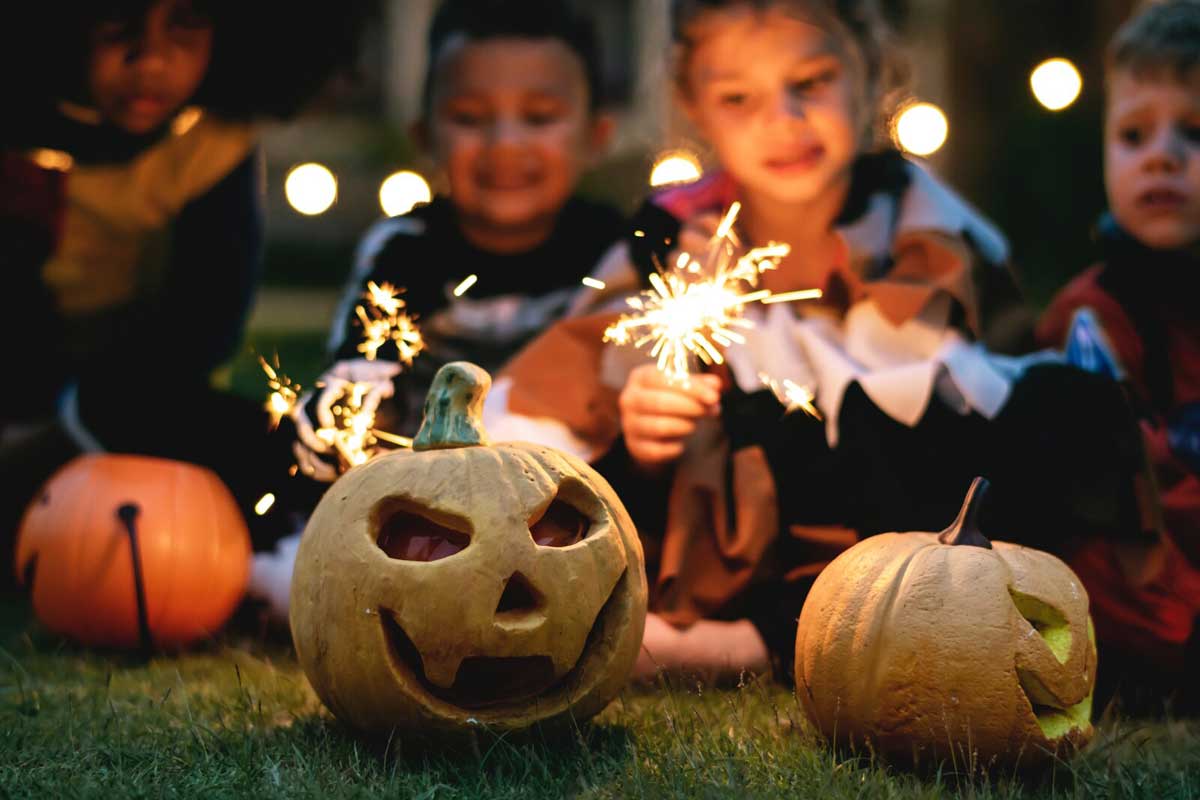 Kids playing with sparklers behind jack o lanterns