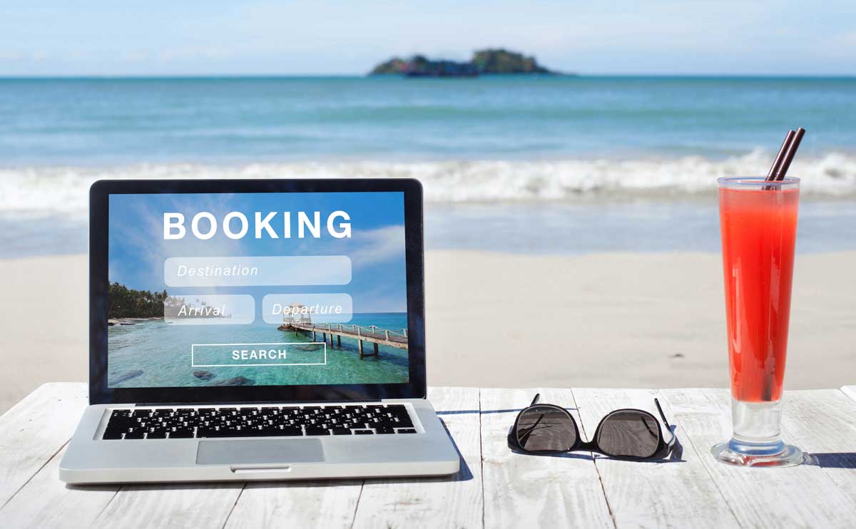 laptop with travel booking on bench beach in background