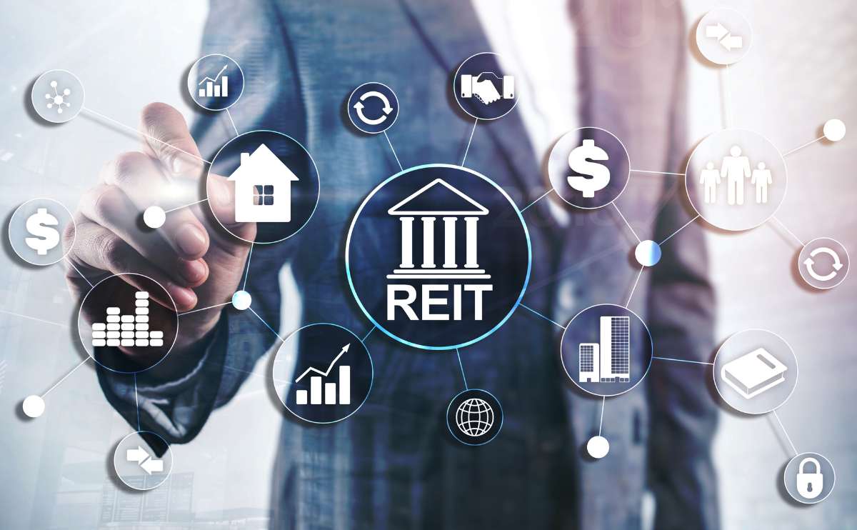 A man in a business suit pointing at graphic showing financial symbols and REIT.