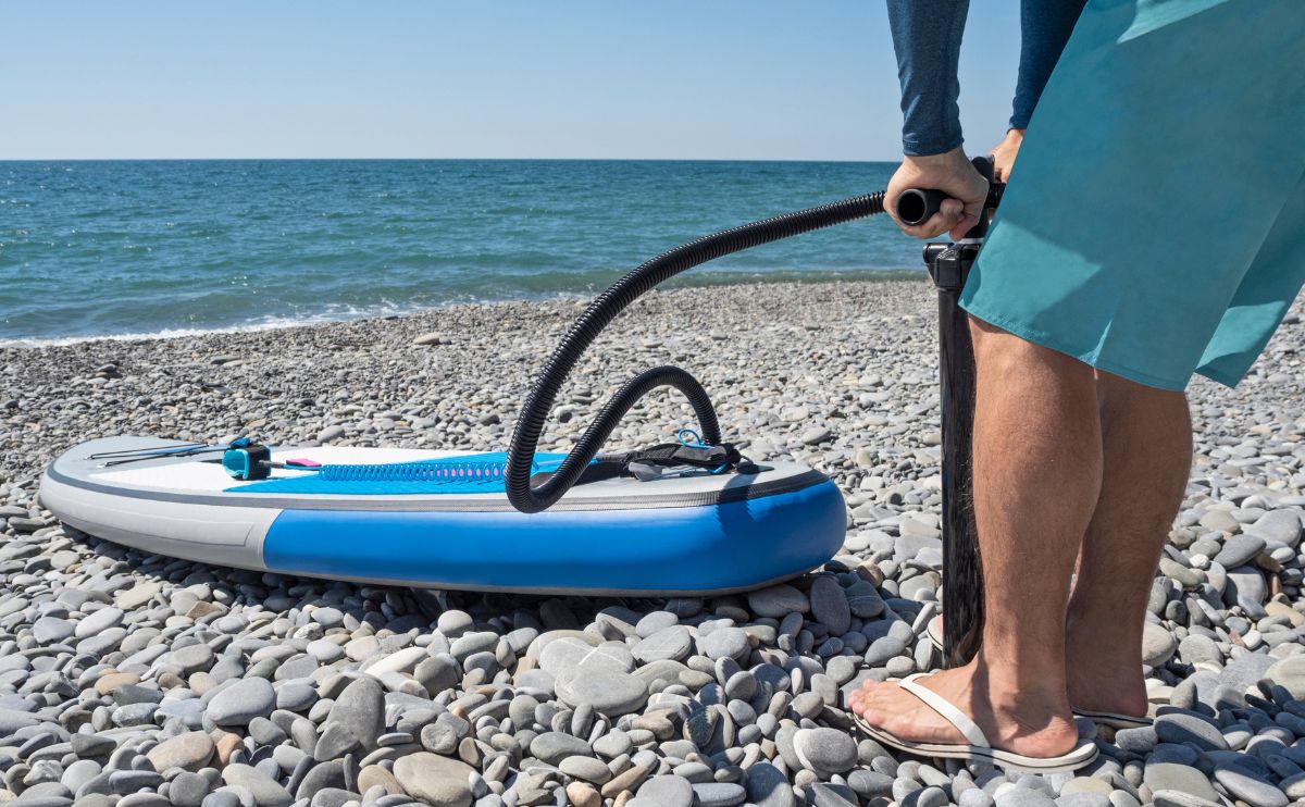 man on beach inflating a paddle board wearing swim trunks jpg