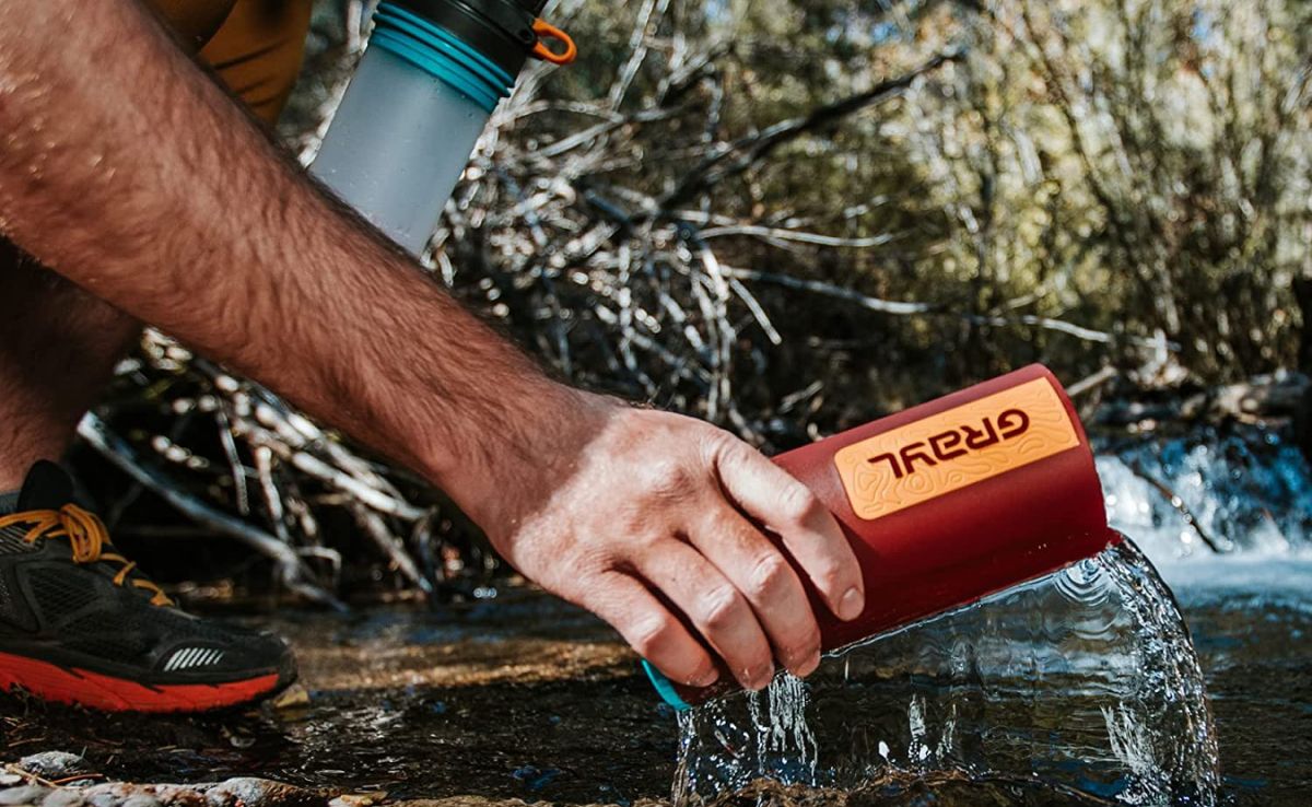 person filling up water bottle from a stream while hiking