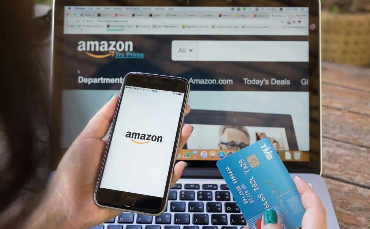 A person shopping online on amazon with phone and credit card in front of computer.