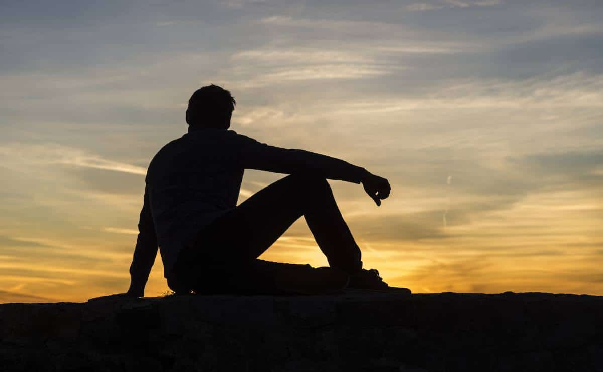 A person silhouette sitting looking at sunset thinking.