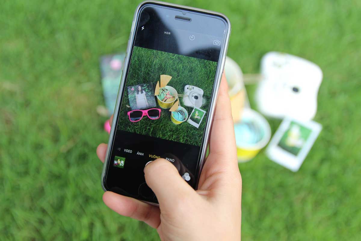 A smartphone taking picture of sunglasses, a photo, and two ice cream cups on grass