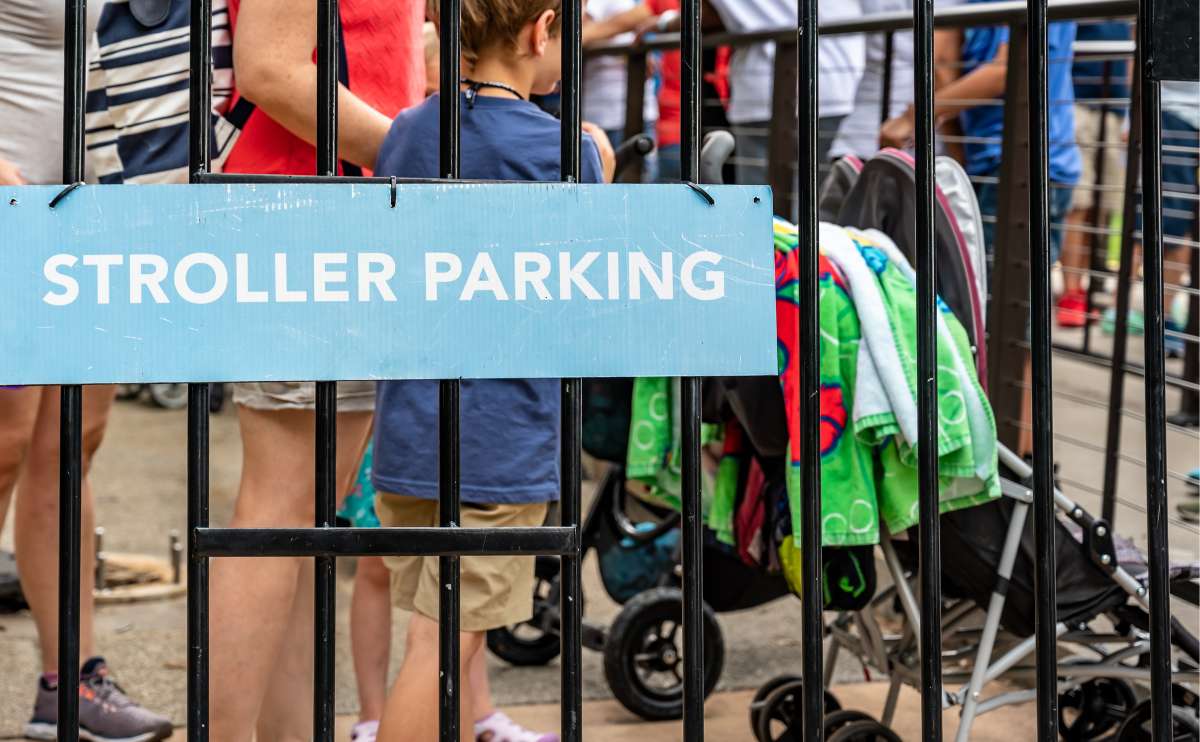 Stroller parking sign posted on a metal fence with people and strollers in the background.