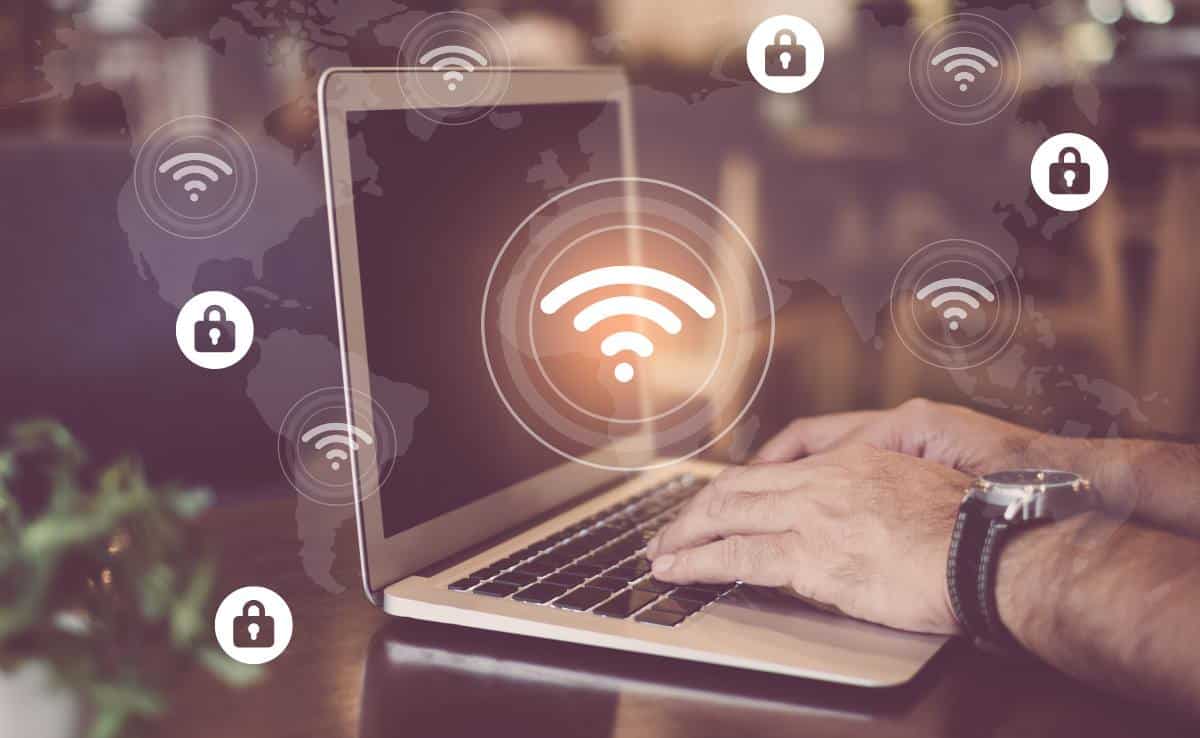 A man's hands typing on a Macbook air with WiFi symbol and map of hotspots and lock icons overlay