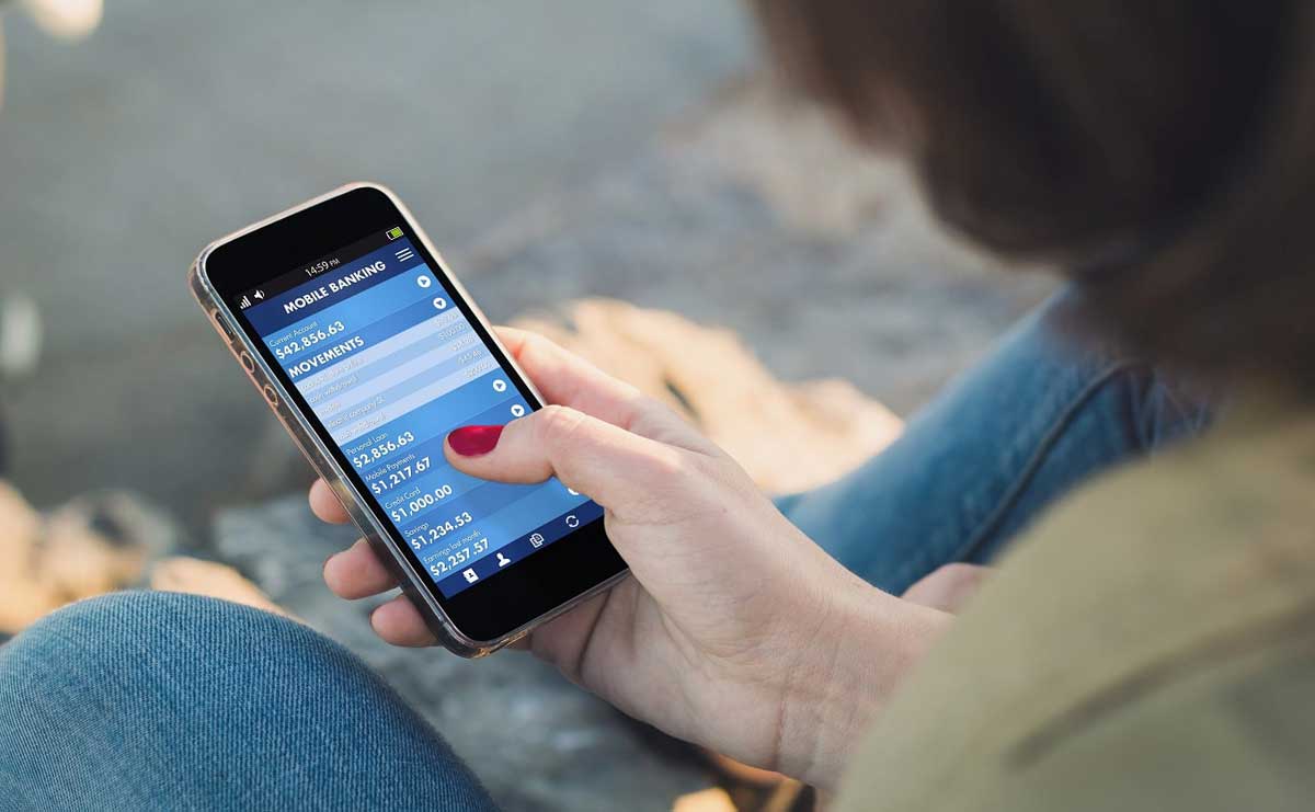 Woman sitting and looking at her smartphone that shows a personal finance app on the screen.