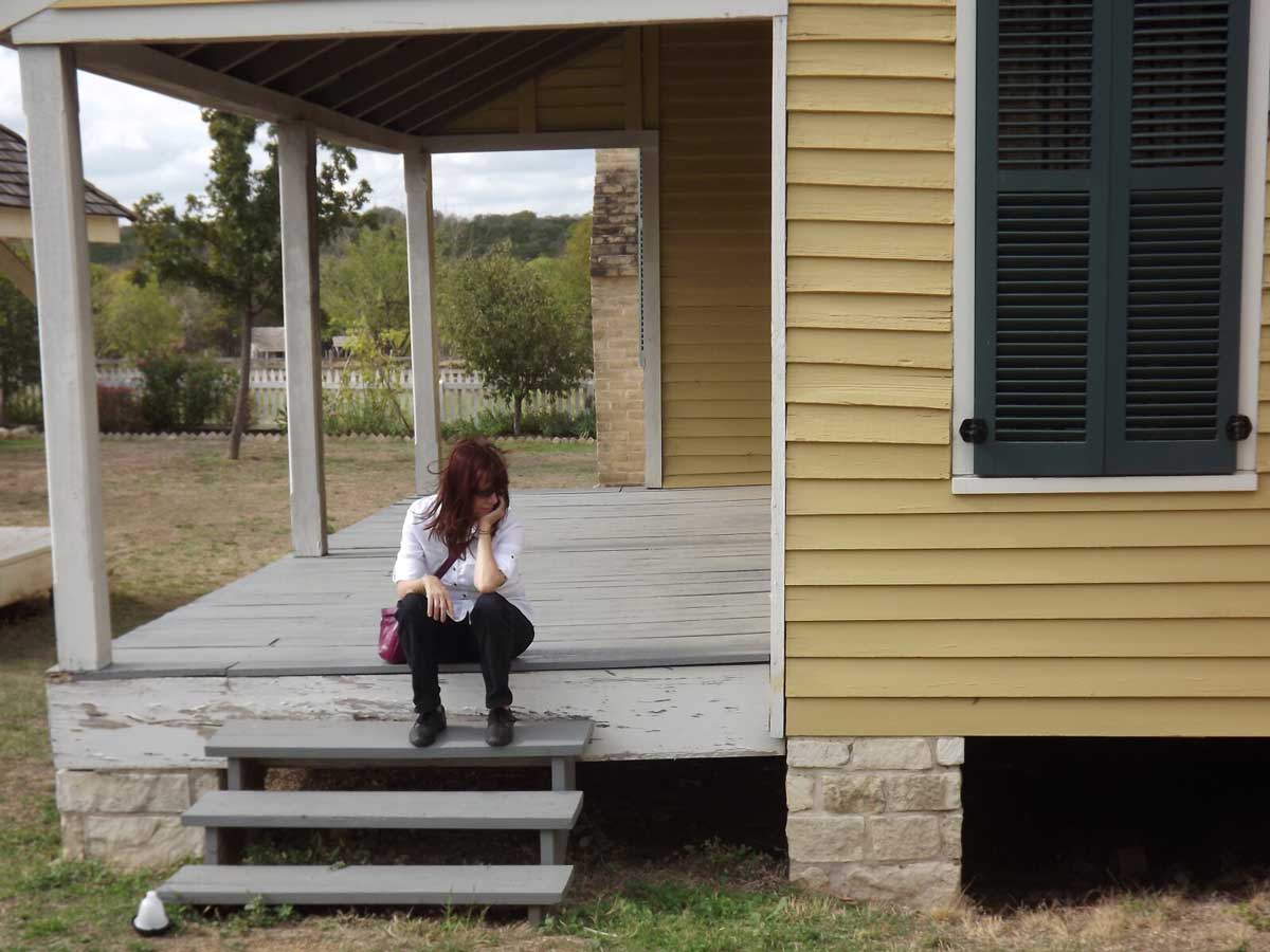 Woman sitting on steps of porch outside house looking downtrodden