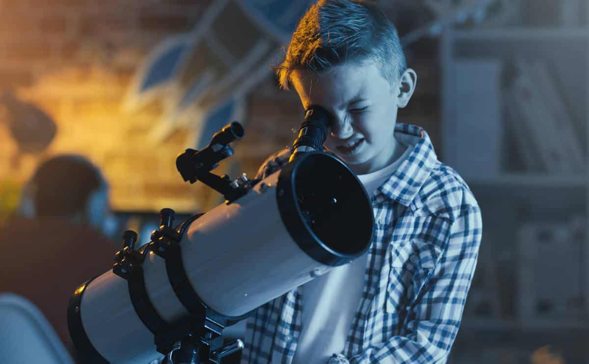 A young person looking at telescope outside.